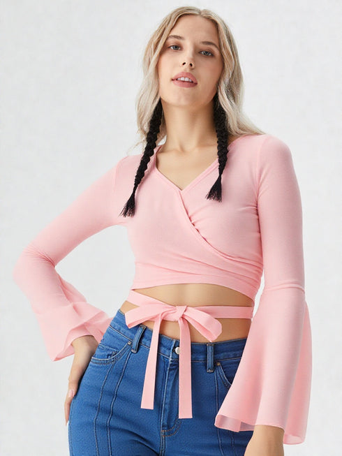 Woman wearing baby pink wrap front bell sleeve crop top with tie waist and blue jeans