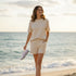 Beige textured co-ord set with short-sleeve top and drawstring shorts worn by a woman walking on the beach