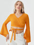 Woman wearing mustard yellow wrap front bell sleeve crop top with tie waist and blue flared jeans