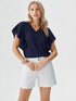Woman wearing navy blue ruffle sleeve V-neck top with white shorts