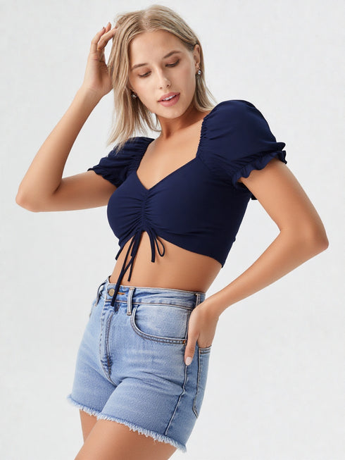 Woman wearing navy blue ruched drawstring puff sleeve crop top with light blue denim shorts