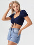 Woman wearing navy blue ruched drawstring puff sleeve crop top with light blue denim shorts