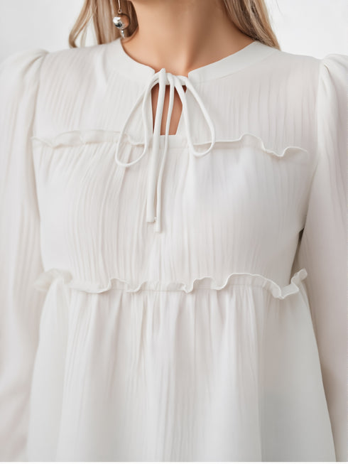 Close-up of woman wearing white ruffle detail tie neck blouse with long sleeves
