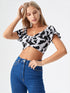 Woman wearing a black and white cow print ruched crop top with puff sleeves and blue jeans