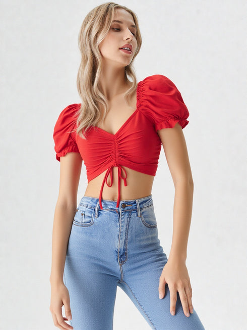 Woman wearing a red puff sleeve ruched crop top paired with light blue denim jeans
