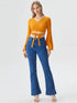 Woman wearing mustard yellow wrap front bell sleeve crop top with tie waist and blue flared jeans