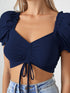 Woman wearing navy blue ruched drawstring puff sleeve crop top with light blue denim shorts