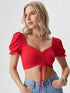 Woman wearing a red puff sleeve ruched crop top paired with light blue denim jeans