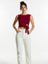 Woman wearing wine red side tie sleeveless crop top with white high-waisted trousers