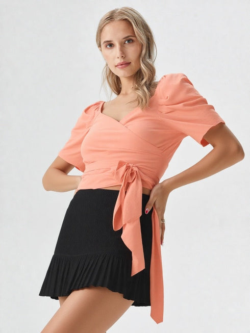 Woman wearing a peach puff sleeve wrap top with tie waist