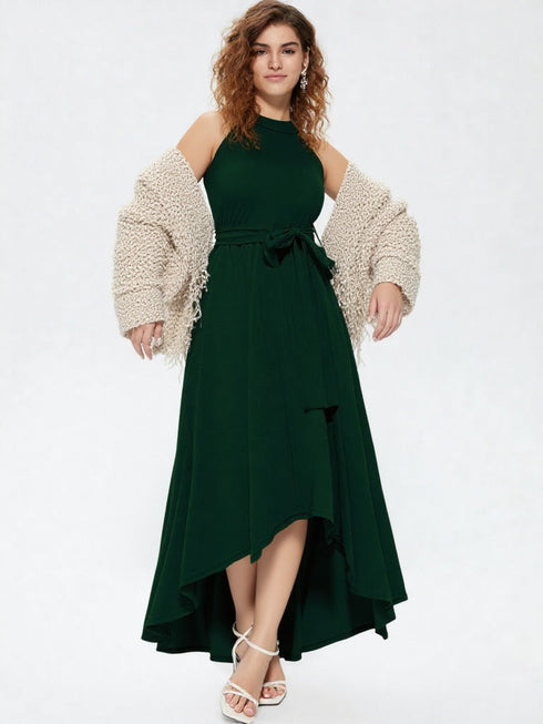 Woman wearing dark green halter neck asymmetrical maxi dress with tie waist belt and white heels