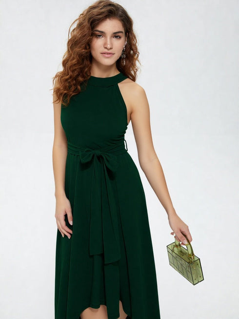 Woman wearing dark green halter neck asymmetrical maxi dress with tie waist belt and white heels