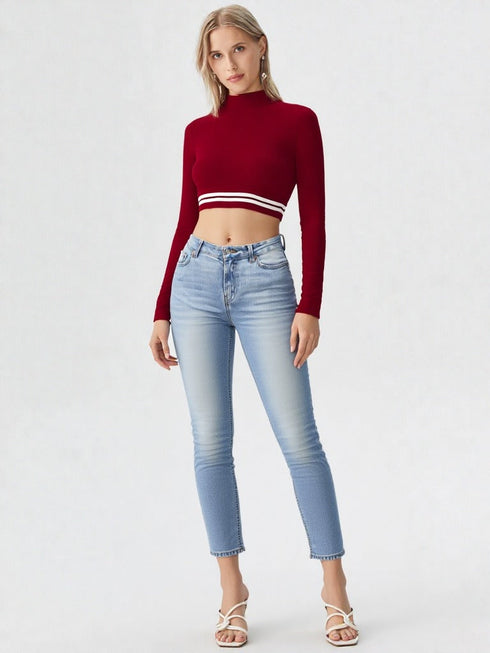 Woman wearing wine red mock neck long sleeve crop top with striped hem paired with denim shorts
