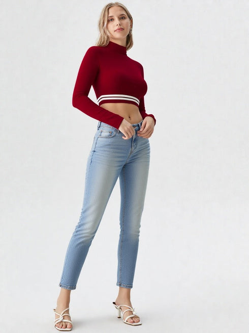 Woman wearing wine red mock neck long sleeve crop top with striped hem paired with denim shorts
