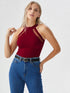 Woman wearing wine red halter neck cutout top with black belt and blue jeans