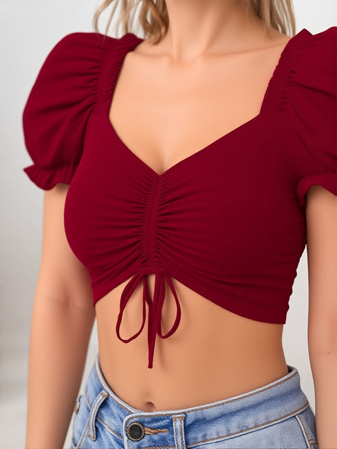Woman wearing a wine red ruched puff sleeve crop top with tie front