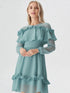 Woman wearing teal ruffle off shoulder long sleeve dress with layered detailing and white heels