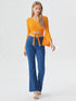 Woman wearing mustard yellow wrap front bell sleeve crop top with tie waist and blue flared jeans