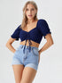 Woman wearing navy blue ruched drawstring puff sleeve crop top with light blue denim shorts
