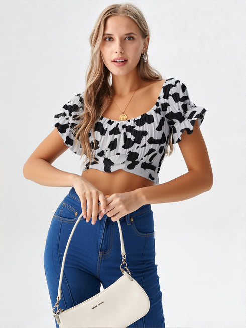 Woman wearing a black and white cow print ruched crop top with puff sleeves and blue jeans