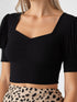 Close-up of woman wearing black sweetheart neck puff sleeve crop top with printed skirt