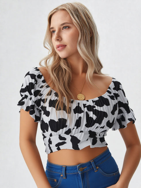 Woman wearing a black and white cow print ruched crop top with puff sleeves and blue jeans