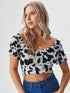 Woman wearing a black and white cow print ruched crop top with puff sleeves and blue jeans