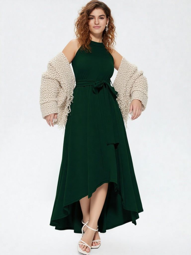 Woman wearing dark green halter neck asymmetrical maxi dress with tie waist belt and white heels  