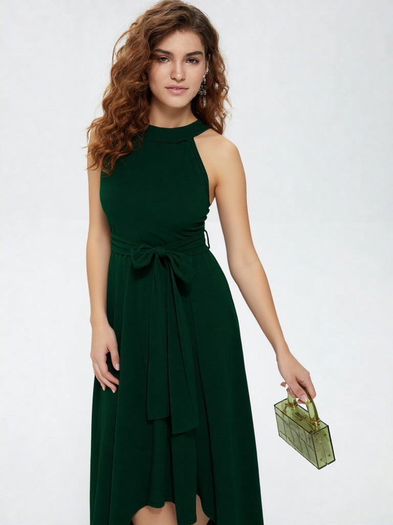 Woman wearing dark green halter neck asymmetrical maxi dress with tie waist belt and white heels  